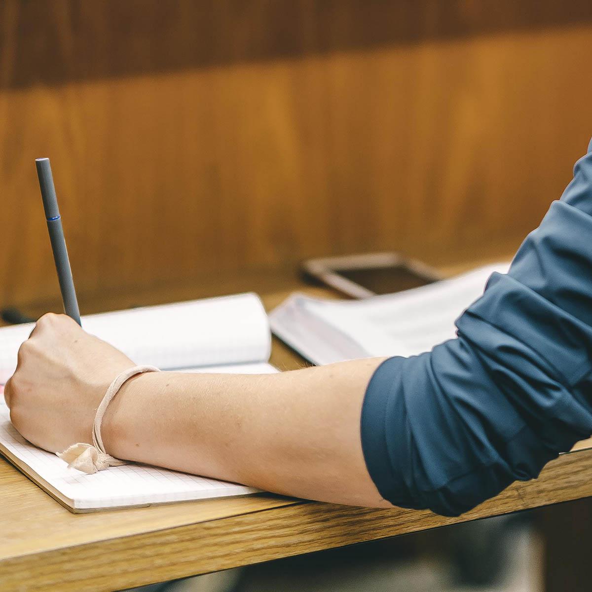 Close-up of a student's hand writing in a notebook on a library table