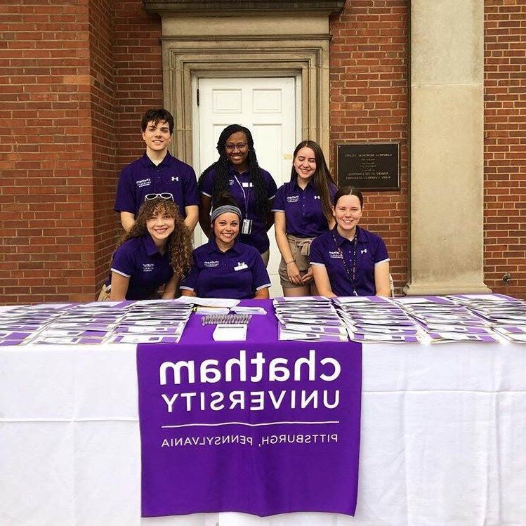 Photo of six Chatham University students in purple shirts, working at a table outside on 足球波胆平台